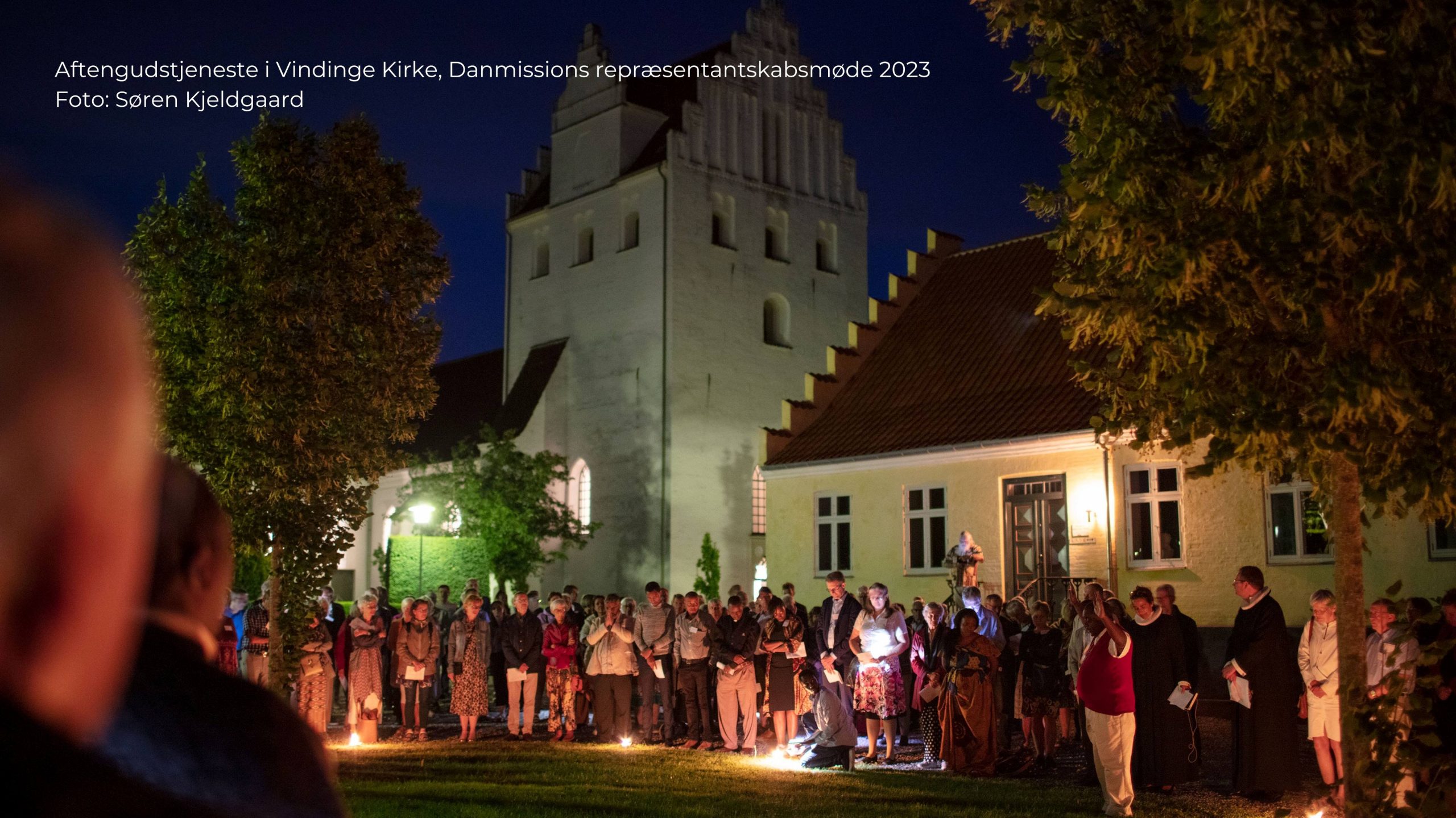 Deltagere i en aftengudstjeneste i Vindinge Kirke på Fyn står udenfor kirken i en cirkel. Der er mørkt og der er tændt havelys.