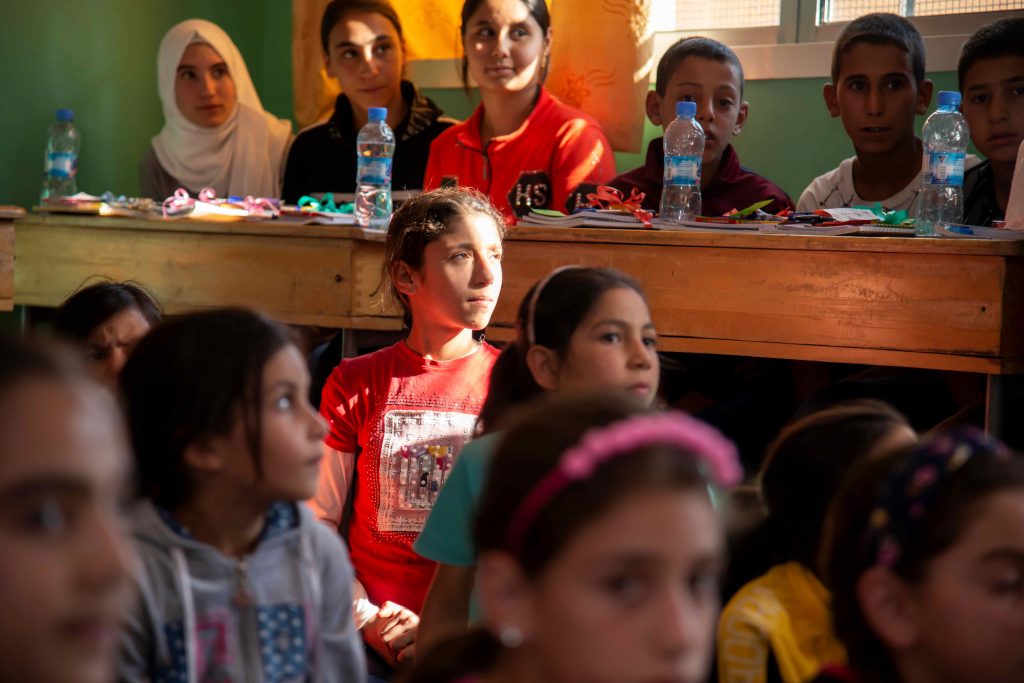 En gruppe af børn i et klasseværelse i et børnecenter i Syrien. En stribe af sol falder på en piges ansigt.